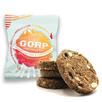 Peanut Butter & Raspberry GORP Clean Energy Bar in it's package. GORP World sticker is orange at the bottom, beginning to lighten in the middle and yellow at the top. Three Peanut Butter & Raspberry GORP Bars are stacked to the right with one bar leaning to the right of the pile. Each bar is 65g.